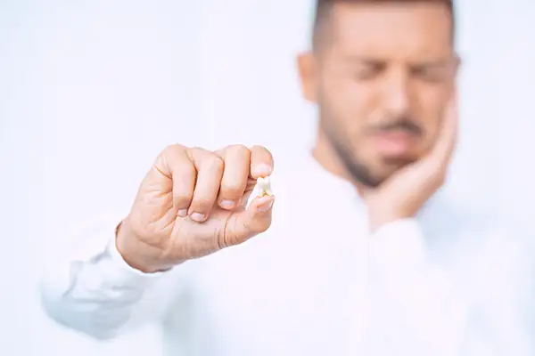 A man holding a wisdom tooth after extraction, wincing and holding his jaw due to impacted wisdom tooth discomfort.